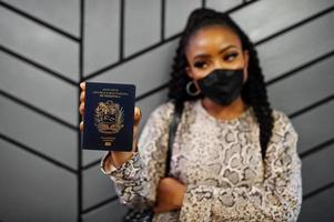 African american woman wearing black face mask show Venezuela passport in hand. Coronavirus in America country, border closure and quarantine, virus outbreak concept. photo