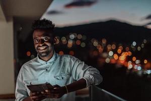 el joven en una calle urbana de la ciudad por la noche enviando mensajes de texto en un teléfono inteligente con bokeh y luces de neón en el fondo. foto