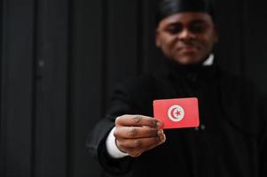 African man wear black durag hold Tunisia flag at hand isolated dark background. photo