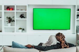 African Couple Sitting On Sofa Watching TV Together Chroma Green Screen Woman Wearing Islamic Hijab Clothes photo