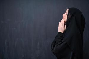 muslim woman making traditional prayer to God in front of black chalkboard