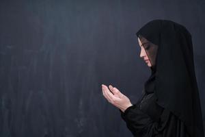 muslim woman making traditional prayer to God in front of black chalkboard photo