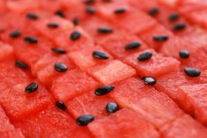 Diced red ripe watermelon in rows, black seeds are scattered on top. Juicy fresh fruit pieces seamless background geometric pattern. Perspective view. Place for text. photo