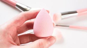 Woman's hand holding a clean makeup sponge with blurred make up brushes in the background photo