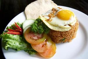 Nasi goreng fried rice with shrimps and egg garnished with fresh cucumber slices and prawn crackers on a white plate . Asian food. photo