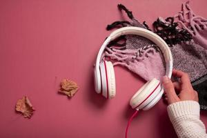 Female hand with headphones and plaid on dark pink color background. Creative music, relax, online concept photo