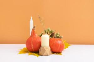 Autumn creative composition. Dried leaves wreath, pumpkins and candle on white orange background. Autumn fall and thanksgiving day concept. Still life photo