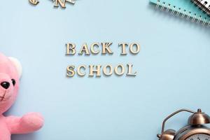 Back to school text with teddy bear, notebook, alarm clock on pastel blue background. Top view, flat lay photo