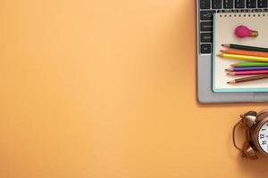 Colorful pencils and note on laptop with alarm clock on colored background. Copy space. Top view, flat lay photo