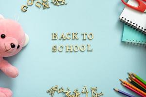 Back to school text with teddy bear and stationary on pastel blue background. Top view, flat lay photo