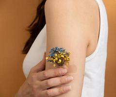 flor azul y amarilla debajo del parche en la mano de una mujer. el concepto de vacunación y tratamiento en ucrania foto