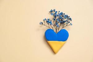Blue and yellow heart and blue flowers on yellow background. Love Ukraine concept photo