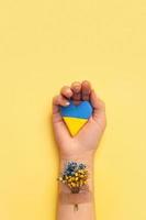 Heart and Blue and yellow flower under the patch on a female hand on a yellow background. Love and pray to Ukraine concept photo