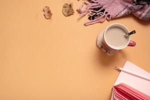 escritorio de vista superior con taza de café, cuaderno y tela escocesa sobre fondo de color. mesa de trabajo de otoño o invierno plana foto