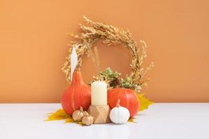 Autumn creative composition. Dried leaves wreath, pumpkins and candle on white orange background. Autumn fall and thanksgiving day concept. Still life photo