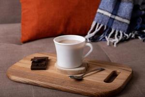 Autumn mood composition with cup of cocoa and chocolate, plaid and books on sofa background. Hot drink in autumn concept photo