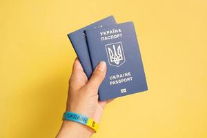 Passports of a citizen of Ukraine in a female hand on a yellow background, close-up. Inscription in Ukrainian Ukraine Passport photo