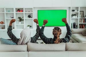 pareja africana sentada en el sofá viendo la televisión juntos pantalla verde croma mujer vistiendo ropa islámica hiyab foto