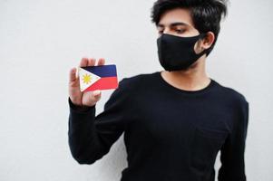 Asian man wear all black with face mask hold Philippines flag in hand isolated on white background. Coronavirus country concept. photo