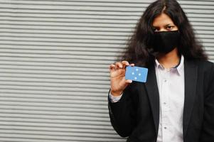 Asian woman at formal wear and black protect face mask hold Micronesia flag at hand against gray background. Coronavirus at country concept. photo