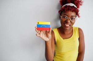 mujer afroamericana con cabello afro, use camiseta amarilla y anteojos, sostenga la bandera de venezuela aislada sobre fondo blanco. foto