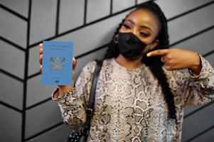 African woman wearing black face mask show Kenya passport in hand. Coronavirus in Africa country, border closure and quarantine, virus outbreak concept. photo