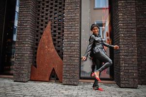 Fashionable beautiful african american woman posing in black leather jacket and pants at street. photo