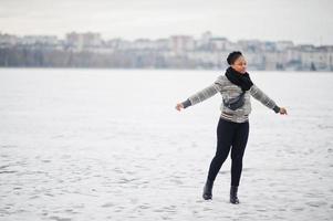 African woman wear in black scarf pose in frozen ice lake, winter day at Europe. photo