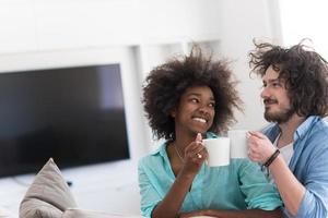 multiethnic couple sitting on sofa at home drinking coffe photo