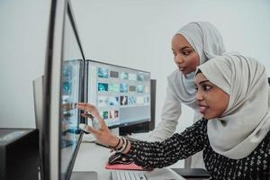 Friends at the office two young Afro American modern Muslim businesswomen wearing scarf in creative bright office workplace with a big screen photo