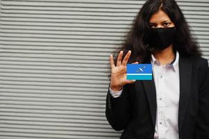 Asian woman at formal wear and black protect face mask hold Midway Atoll flag at hand against gray background. Coronavirus at country concept. photo