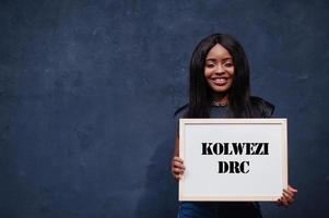 mujer africana sostiene una pizarra blanca con la inscripción kolwezi drc. concepto de ciudad más poblada de África. foto