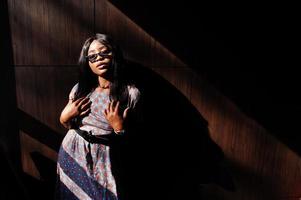 Game with shadows. Fashion portrait of african american woman in long dress and eyeglasses indoor. photo