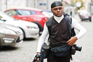 Young professional african american videographer holding professional camera with tripod pro equipment. Afro cameraman wearing black duraq making a videos. photo