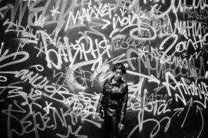 Fashionable beautiful african american woman posing in black leather jacket and pants at street against graffiti wall. photo