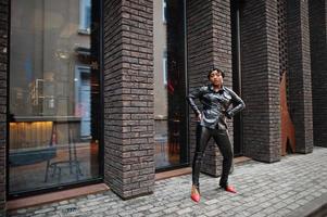 Fashionable beautiful african american woman posing in black leather jacket and pants at street. photo