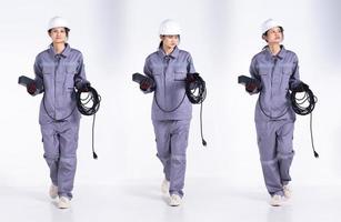 Full length 20s young Mix Race engineer electrician Woman, walking forward left right, wear gray uniform. Contractor female hold electric plug cable smile happy over white background isolated photo