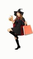 Beautiful girl in black dress and witch hat is holding pumpkin with shopping bags and smiling on white background for Halloween day. with wow emotion photo