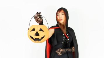 linda chica asiática hermosa con cabello negro y naranja en vestido negro y sombrero de bruja sostiene calabaza. foco calabaza concepto halloween. foto