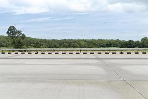 vista horizontal del camino concreto vacío con la cerca del borde de la carretera en Tailandia. fondo de árboles bajo el cielo azul con nubes blancas. foto