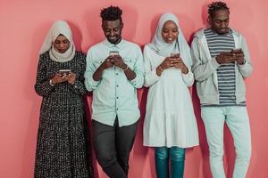 A group of African Muslim students use smartphones while standing in front of a pink background photo