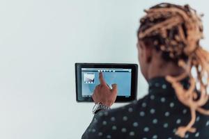 Smiling African American man using modern smart home system, controller on wall, positive young man switching temperature on thermostat or activating security alarm in apartment photo