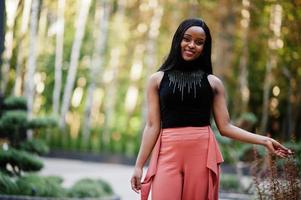 Fashionable african american woman in peach pants and black blouse pose outdoor. photo