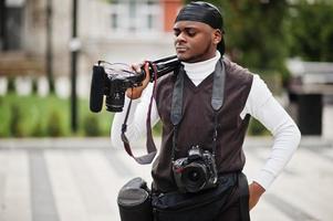 Young professional african american videographer holding professional camera with pro equipment. Afro cameraman wearing black duraq making a videos. photo