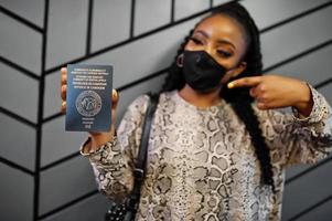 African woman wearing black face mask show Cameroon passport in hand. Coronavirus in Africa country, border closure and quarantine, virus outbreak concept. photo