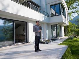 man using mobile phone in front of his luxury home villa photo