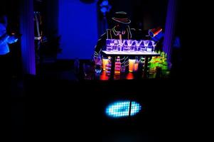 Professional barman and led light show. Silhouette of modern bartender shaking drink at night cocktail bar. photo