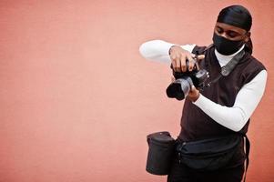 Young professional african american videographer holding professional camera with pro equipment. Afro cameraman wearing black duraq and face protect mask, making a videos. photo