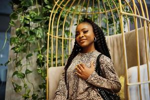 Young stylish african american woman in gold bird cage pose indoor. photo