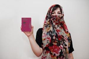 joven musulmana árabe vestida con hijab tiene pasaporte de la república de chipre sobre fondo de pared blanca, retrato de estudio. foto